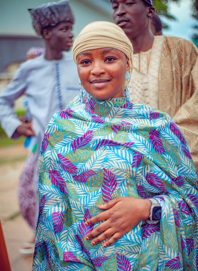 A woman in colorful traditional attire smiles during a cultural gathering outdoors.
